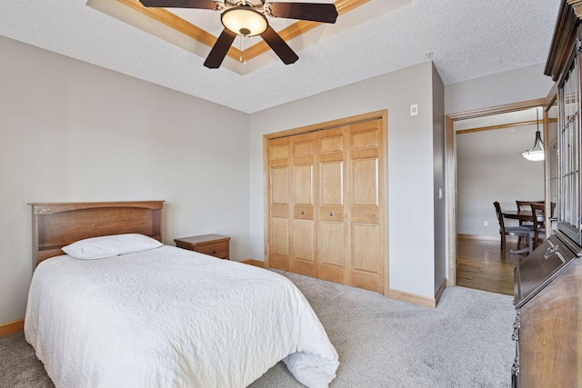 carpeted bedroom with a closet, ceiling fan, a textured ceiling, and baseboards