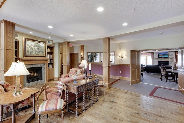 living area featuring light wood finished floors, a fireplace, ornate columns, and a textured ceiling