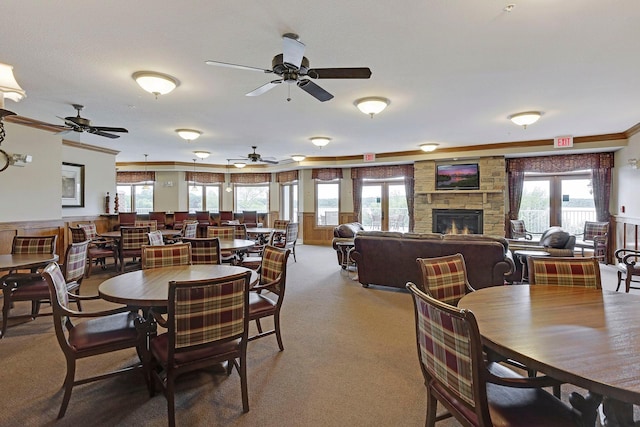 dining room with a stone fireplace, crown molding, and carpet flooring