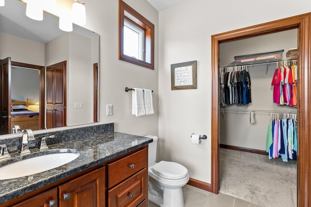 bathroom featuring vanity, baseboards, tile patterned flooring, a walk in closet, and toilet