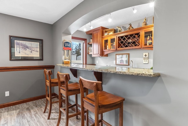 bar featuring light wood-type flooring, a sink, arched walkways, indoor wet bar, and baseboards