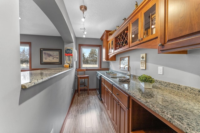 kitchen featuring dishwashing machine, light stone countertops, a sink, a textured ceiling, and light wood-type flooring