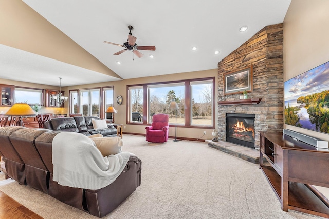 living area with baseboards, high vaulted ceiling, recessed lighting, a stone fireplace, and ceiling fan with notable chandelier