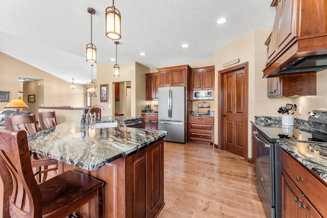 kitchen with light wood finished floors, a breakfast bar, dark stone countertops, appliances with stainless steel finishes, and a sink