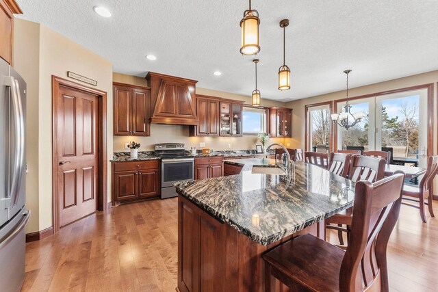 kitchen featuring a kitchen bar, custom range hood, a sink, appliances with stainless steel finishes, and light wood finished floors