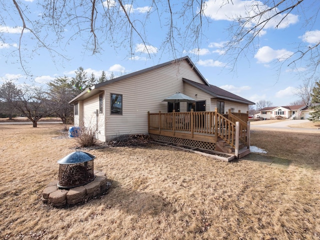 back of property with a wooden deck, a garage, and an outdoor fire pit