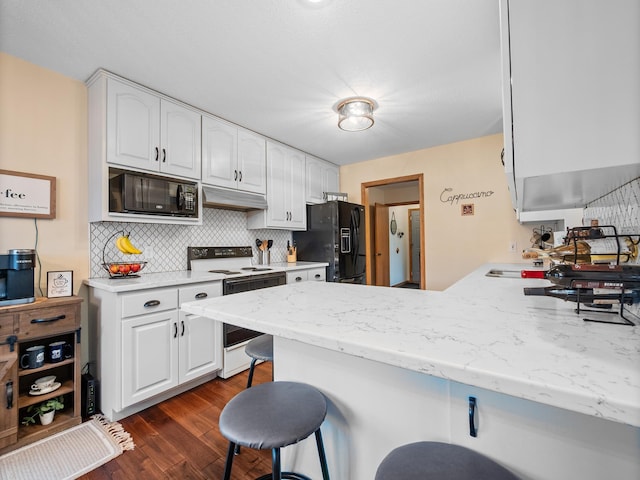 kitchen featuring under cabinet range hood, a breakfast bar area, a peninsula, white cabinets, and black appliances