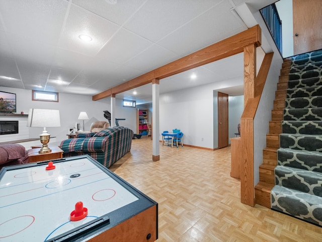 recreation room featuring baseboards, a paneled ceiling, and a fireplace with raised hearth