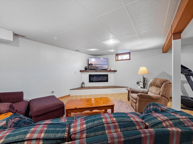 living area with visible vents, a paneled ceiling, and a glass covered fireplace