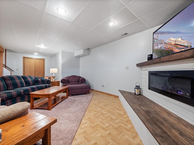 living room featuring a glass covered fireplace, visible vents, a paneled ceiling, and baseboards