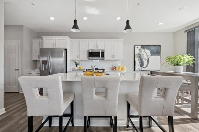 kitchen featuring stainless steel appliances, wood finished floors, light countertops, decorative backsplash, and a center island with sink