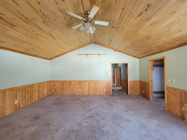 carpeted empty room featuring wooden ceiling, a wainscoted wall, wooden walls, and vaulted ceiling