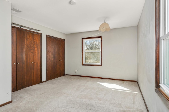 unfurnished bedroom with two closets, visible vents, baseboards, and carpet