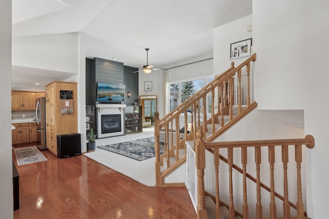 staircase featuring a glass covered fireplace, vaulted ceiling, wood finished floors, and ceiling fan