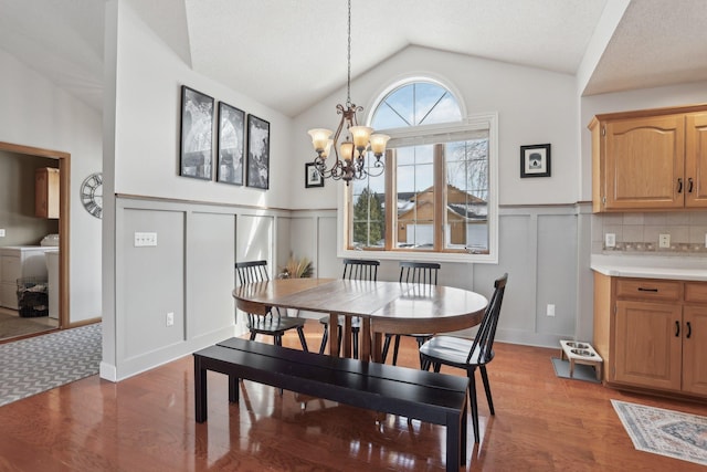 dining area featuring light wood finished floors, an inviting chandelier, a decorative wall, lofted ceiling, and washer / dryer