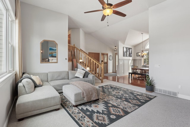 living room with visible vents, stairs, lofted ceiling, carpet flooring, and ceiling fan with notable chandelier