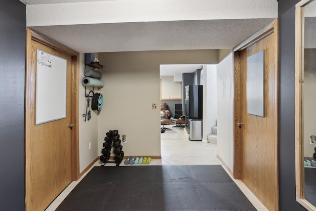 hall featuring light tile patterned floors, a textured ceiling, and baseboards