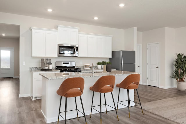 kitchen with stainless steel appliances, white cabinets, a center island with sink, and light wood finished floors