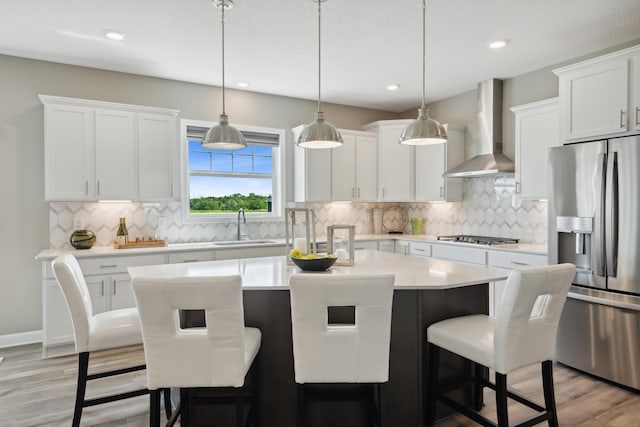 kitchen featuring stainless steel appliances, a sink, wall chimney range hood, a center island, and a kitchen bar