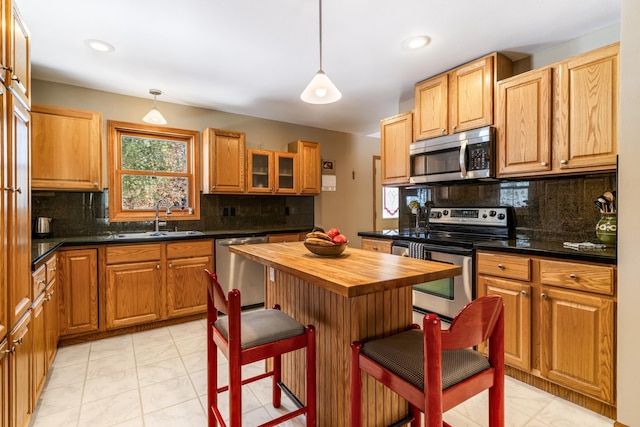 kitchen with wood counters, appliances with stainless steel finishes, a breakfast bar, a sink, and backsplash