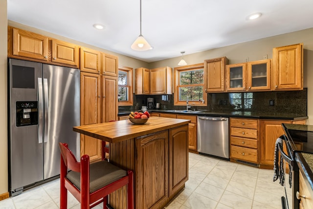 kitchen featuring stainless steel appliances, butcher block countertops, a sink, decorative backsplash, and glass insert cabinets