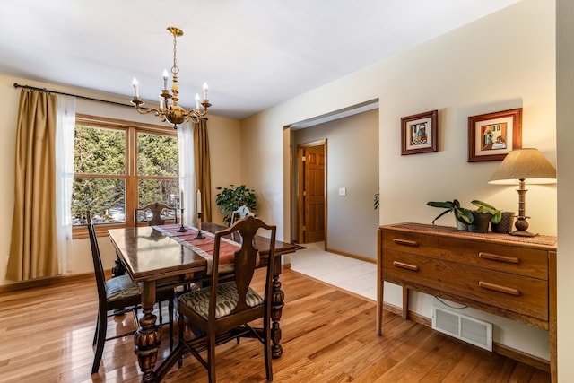 dining room with light wood finished floors, baseboards, visible vents, and an inviting chandelier