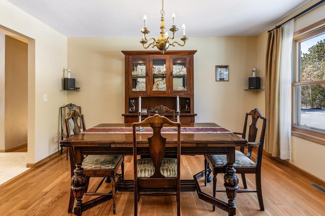 dining area featuring light wood finished floors, visible vents, baseboards, and a notable chandelier