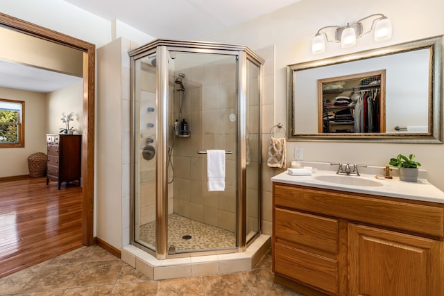 bathroom featuring baseboards, tile patterned flooring, a walk in closet, vanity, and a shower stall