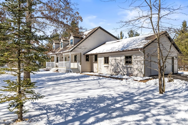 snow covered property with covered porch and an attached garage