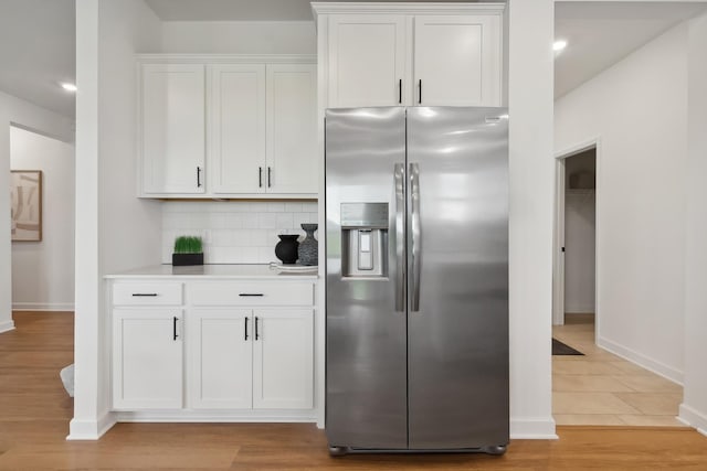 kitchen with white cabinets, decorative backsplash, stainless steel fridge with ice dispenser, light countertops, and light wood-style floors