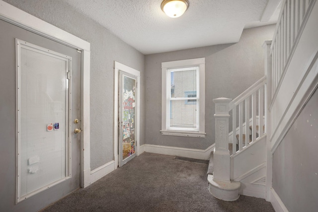 carpeted foyer entrance with a textured ceiling, baseboards, and stairs