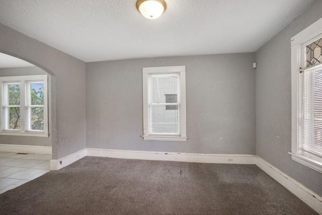 carpeted empty room with arched walkways, tile patterned flooring, a textured ceiling, and baseboards