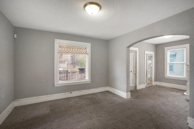 carpeted spare room featuring arched walkways, a textured ceiling, baseboards, and a healthy amount of sunlight