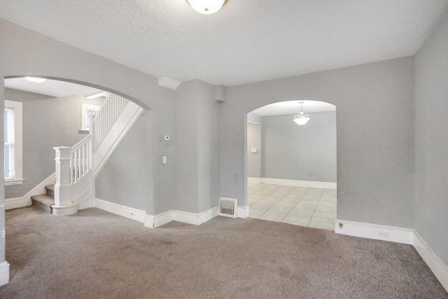 carpeted empty room with arched walkways, a textured ceiling, visible vents, baseboards, and stairs