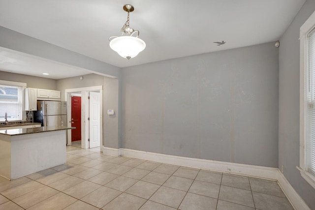 kitchen with decorative light fixtures, freestanding refrigerator, white cabinetry, a sink, and baseboards