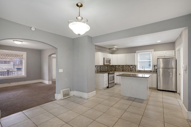 kitchen featuring arched walkways, stainless steel appliances, a sink, visible vents, and decorative backsplash