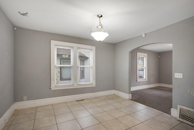 empty room with arched walkways, light tile patterned floors, and a healthy amount of sunlight