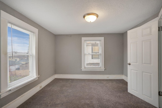 carpeted spare room featuring a textured ceiling and baseboards