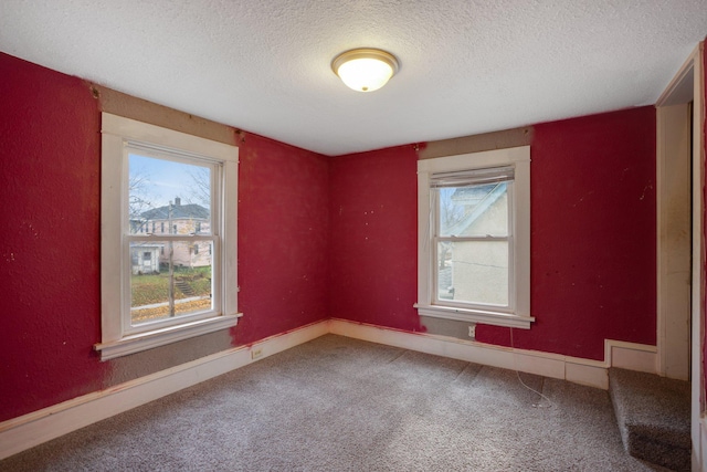 carpeted spare room featuring a textured ceiling, a wealth of natural light, and baseboards