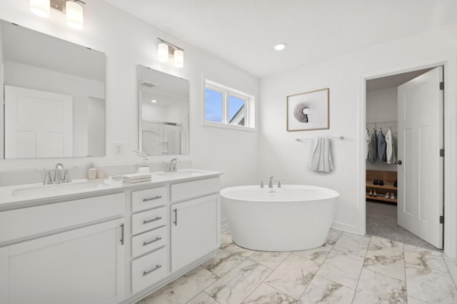 bathroom with marble finish floor, double vanity, a soaking tub, and a sink