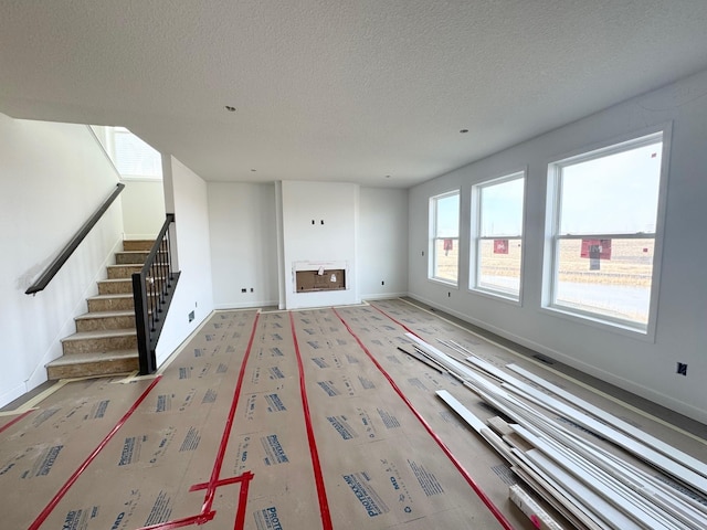 unfurnished living room with stairway, baseboards, and a textured ceiling