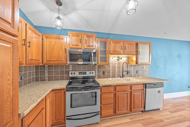 kitchen featuring light wood-style flooring, a sink, backsplash, stainless steel appliances, and glass insert cabinets