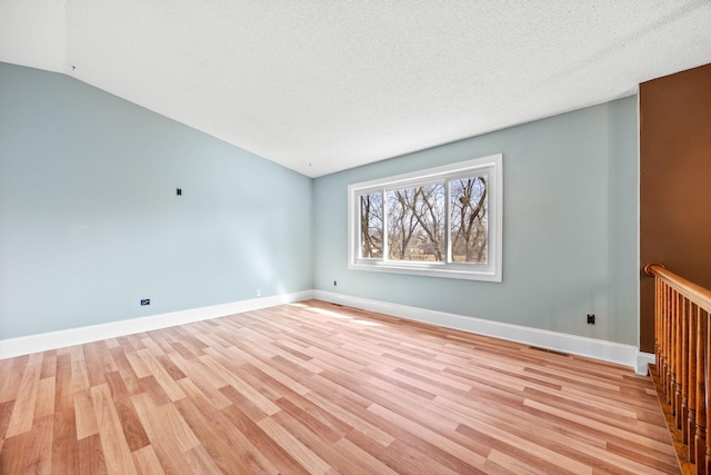 spare room with light wood finished floors, a textured ceiling, and baseboards