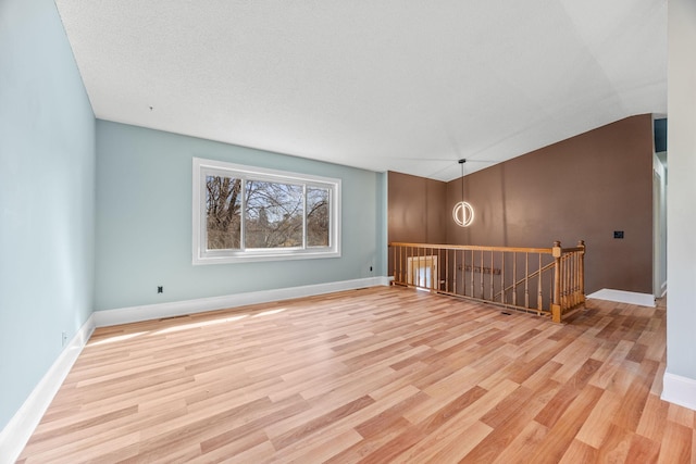 empty room with a textured ceiling, baseboards, and wood finished floors