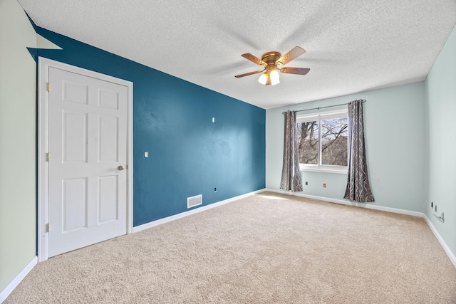 empty room featuring a ceiling fan, visible vents, carpet floors, baseboards, and a textured ceiling