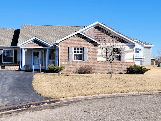 view of front facade with roof with shingles, a front lawn, and brick siding