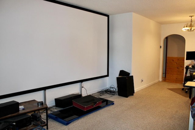 carpeted home theater featuring arched walkways, a textured ceiling, a chandelier, and baseboards