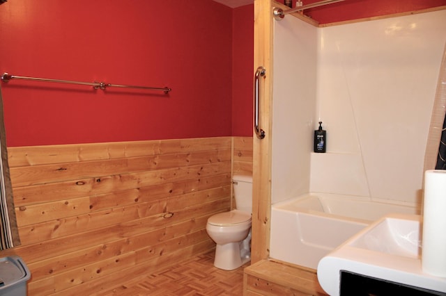 full bathroom with washtub / shower combination, wood walls, wainscoting, and toilet