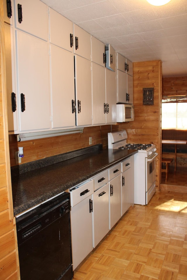 kitchen with dark countertops, white appliances, white cabinets, and wood walls