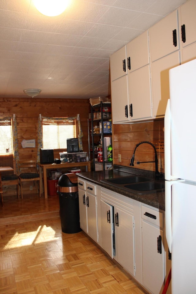 kitchen featuring freestanding refrigerator, white cabinetry, a sink, and dark countertops